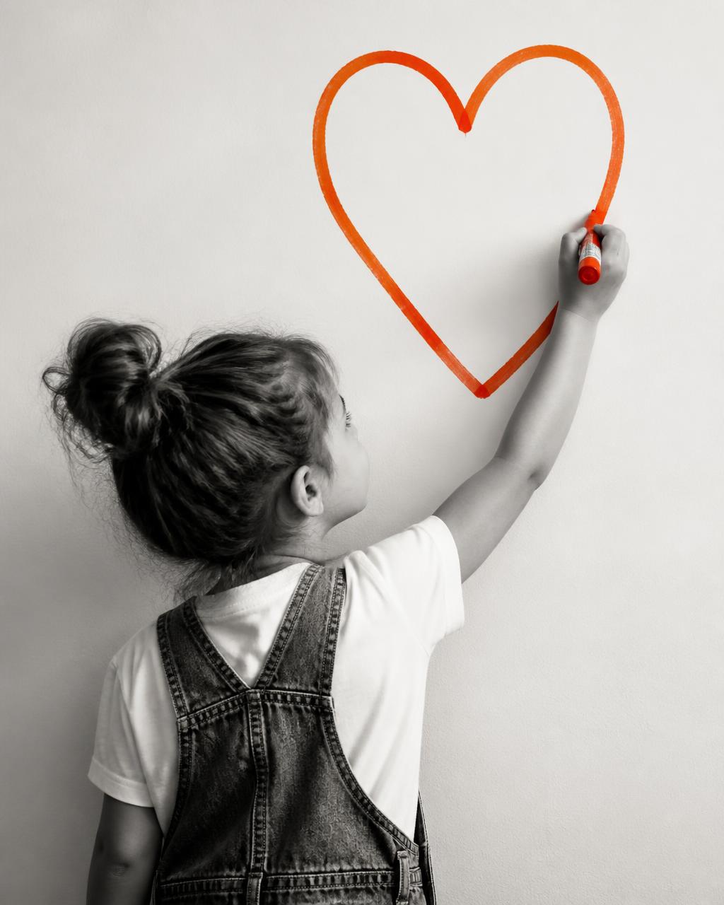 A child drawing a large heart on a wall with an orange marker